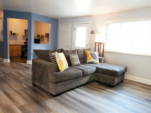 A living room with a sectional sofa, a desk, and a bookshelf. - Your Boulder Home Base, Walk to Pearl St, 2BR/2BA + Parking! (Boulder)