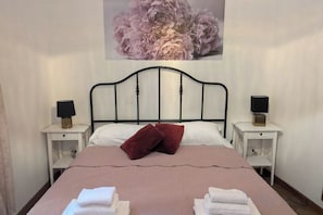 A bed with a headboard, two bedside tables with lamps, a red pillow, and a wall-mounted flower painting. - Gracchi 278 - The Italian Stay Collection (Rome)