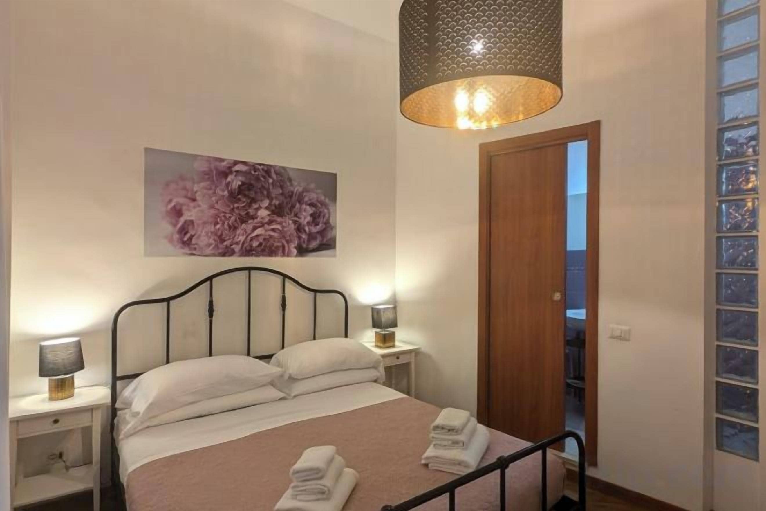 Quarto com cama, luminárias de cabeceira, uma porta e uma janela.