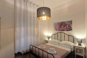 A bedroom with a bed, bedside lamps, a hanging light fixture, and a floral artwork on the wall. - Gracchi 278 - The Italian Stay Collection (Rome)