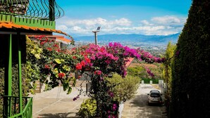 A street with a parked car, a green building, and a view of the city and mountains in the background. - Room just 20 minutes from the airport. (Alajuela)