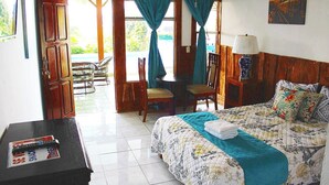 A hotel room with a bed, a desk, a chair, and a table. There is a window with curtains, a painting on the wall, and a view of the outside. - Room just 20 minutes from the airport. (Alajuela)