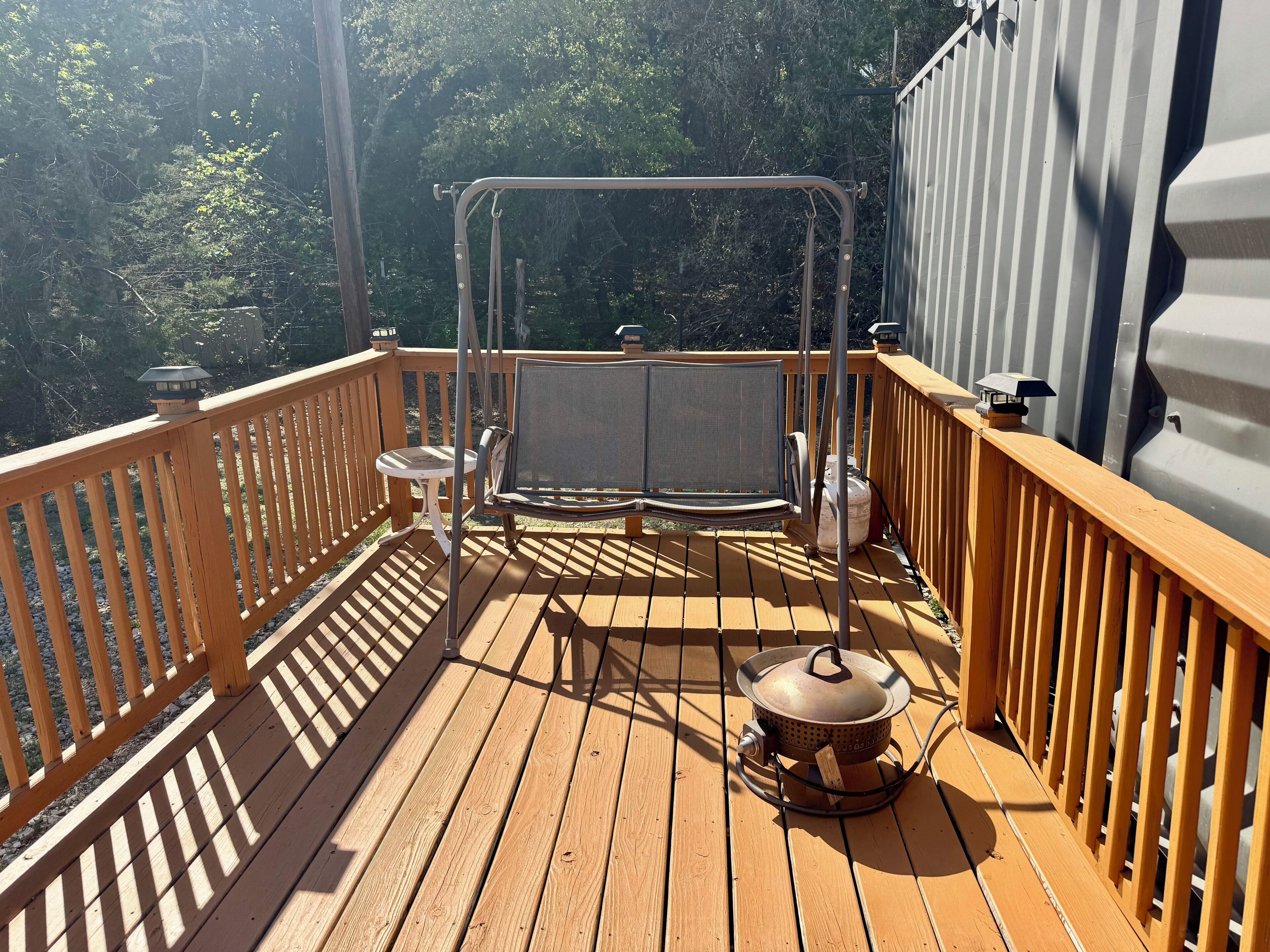 Una terraza de madera con una silla mecedora, una mesita y una estufa portátil.