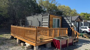 Una construcción pequeña de un piso con terraza de madera y puerta corredera.