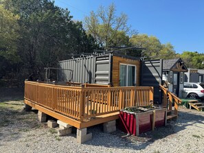 A small, single-story structure with a wooden deck and a sliding door. - Barrel Cactus Container Home (Azle)