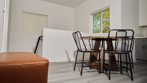A dining area with a round table, four chairs, and a brown leather ottoman. - Modern 5BR 5BA House near USC/DTLA (Los Angeles)