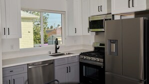 A modern kitchen with white cabinets, stainless steel appliances, and a window providing a view of the outside. - Modern 5BR 5BA House near USC/DTLA (Los Angeles)