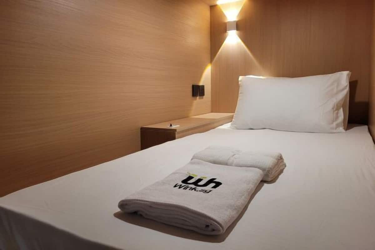 Une chambre d’hôtel avec un lit bien fait, une table de chevet et un luminaire fixé au mur.