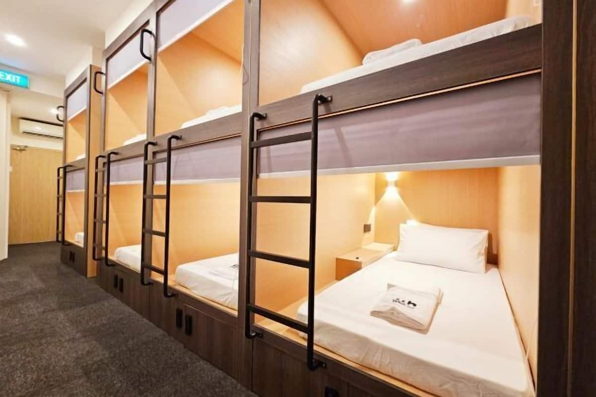 Une chambre d’hôtel avec des lits superposés, un plancher en bois, une table de chevet et une lampe fixée au mur.