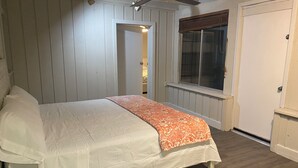 Een slaapkamer met een bed, houten hoofdeinde, witte muren, een raam met jaloezieën en een plafondventilator.