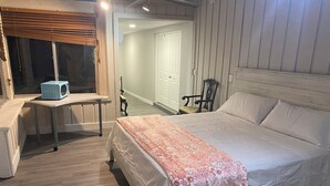 Een slaapkamer met een bed, een bureau, een stoel en een raam met jaloezieën.