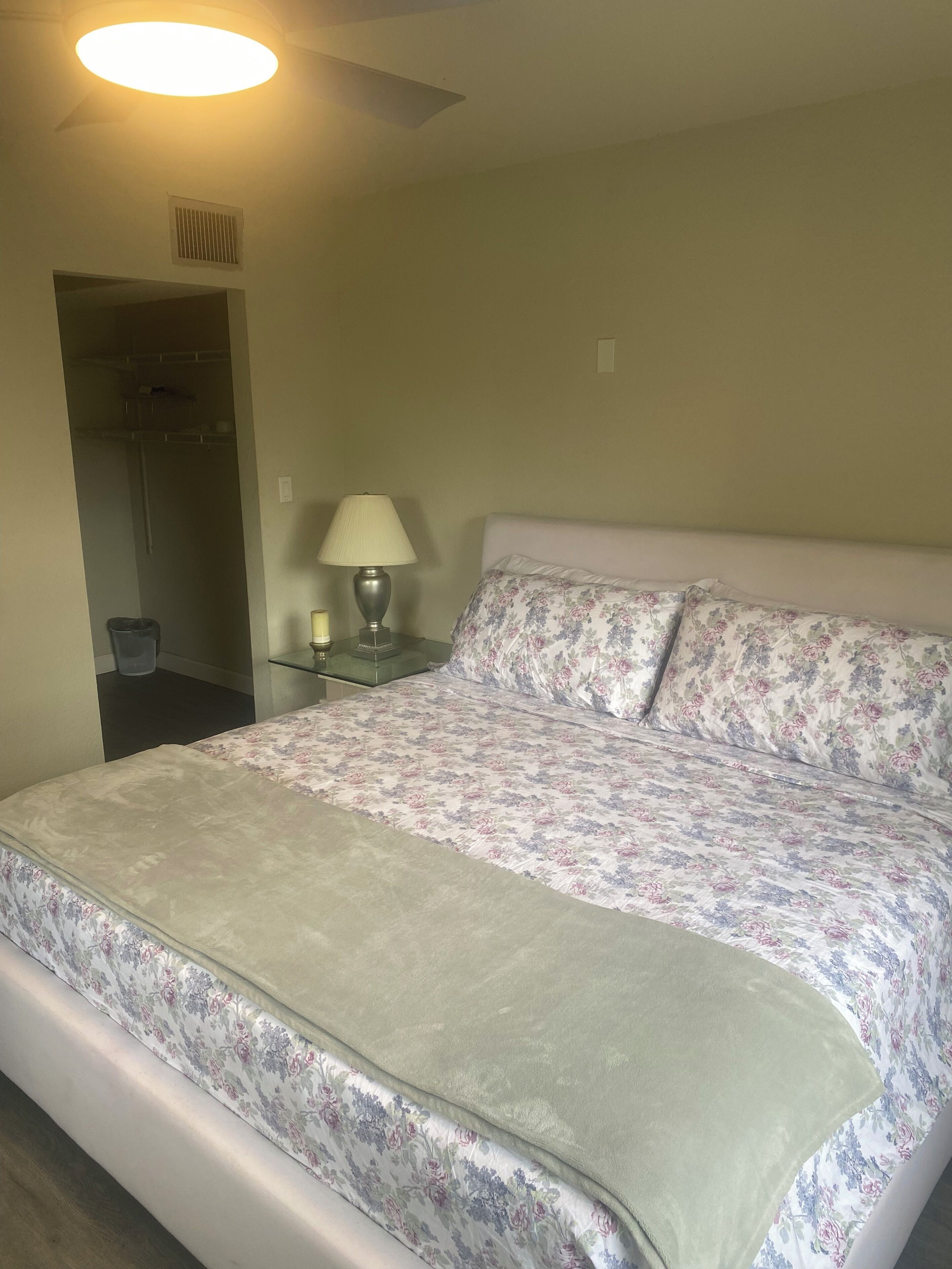 A neatly made bed with floral bedding, a bedside lamp, and a ceiling fan.