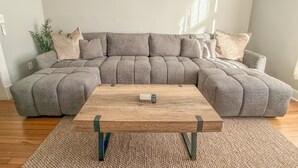 Un sofá modular con una mesa de centro de madera, una alfombra tejida y una planta en la esquina.