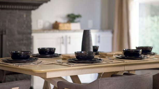 Una mesa vestida con cuencos y platos negros, un alto jarrón negro y una mesa de madera.