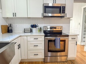 Uma cozinha moderna com armários brancos, micro-ondas de aço inoxidável, torradeira e fogão.
