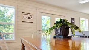 Et træspisebord med en vævet plantekasse, en hvid stol, og et skilt på væggen med teksten 'Welcome to the Lake'.