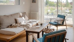 A cozy living room with a sofa, a wooden coffee table, and a chair. There is a window with a view of the outdoors. - Le Petit Civry - SAINT JULIEN DE CIVRY (SAINT JULIEN DE CIVRY)