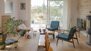 A cozy living room with a wooden table, comfortable seating, a fireplace, and a large window offering a view of the outdoors. - Le Petit Civry - SAINT JULIEN DE CIVRY (SAINT JULIEN DE CIVRY)
