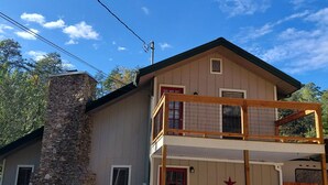 Un bâtiment à deux étages, doté d’une cheminée en pierre, d’une porte rouge et d’un balcon avec des balustrades en bois.