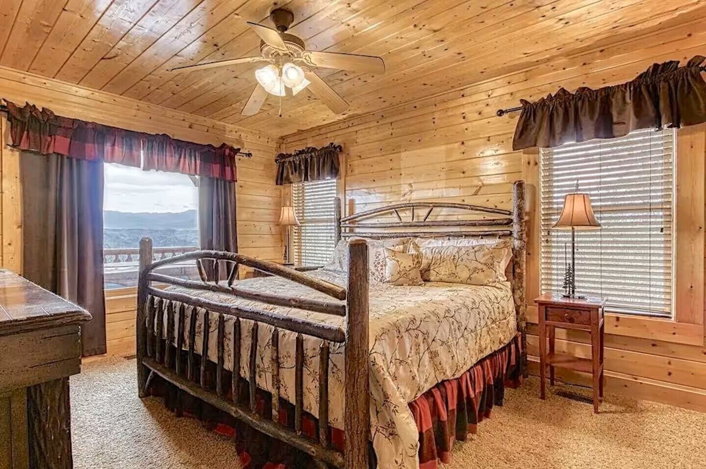 A wooden cabin bedroom with a bed, a nightstand, a lamp, and a view of the outdoors.
