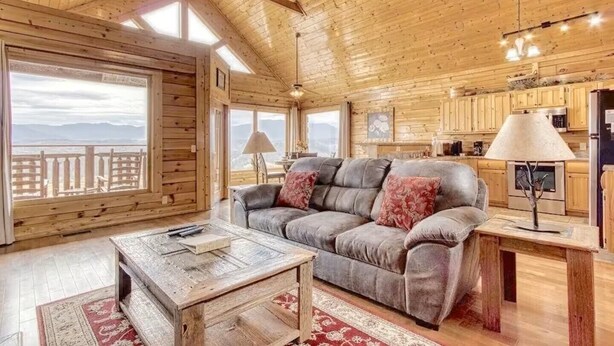 Een gezellig chalet met een houten inrichting, een bank met kussens, een eettafel en uitzicht door grote ramen.
