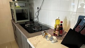 A kitchen with a gas stove, a shelf with kitchen items, and a countertop with a few bottles and a black bag. - Casa Budi Dwiputra 15 Putrajaya (Putrajaya)