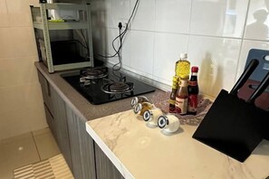 Uma cozinha com fogão a gás, uma prateleira com utensílios de cozinha e bancada com algumas garrafas e uma bolsa preta.