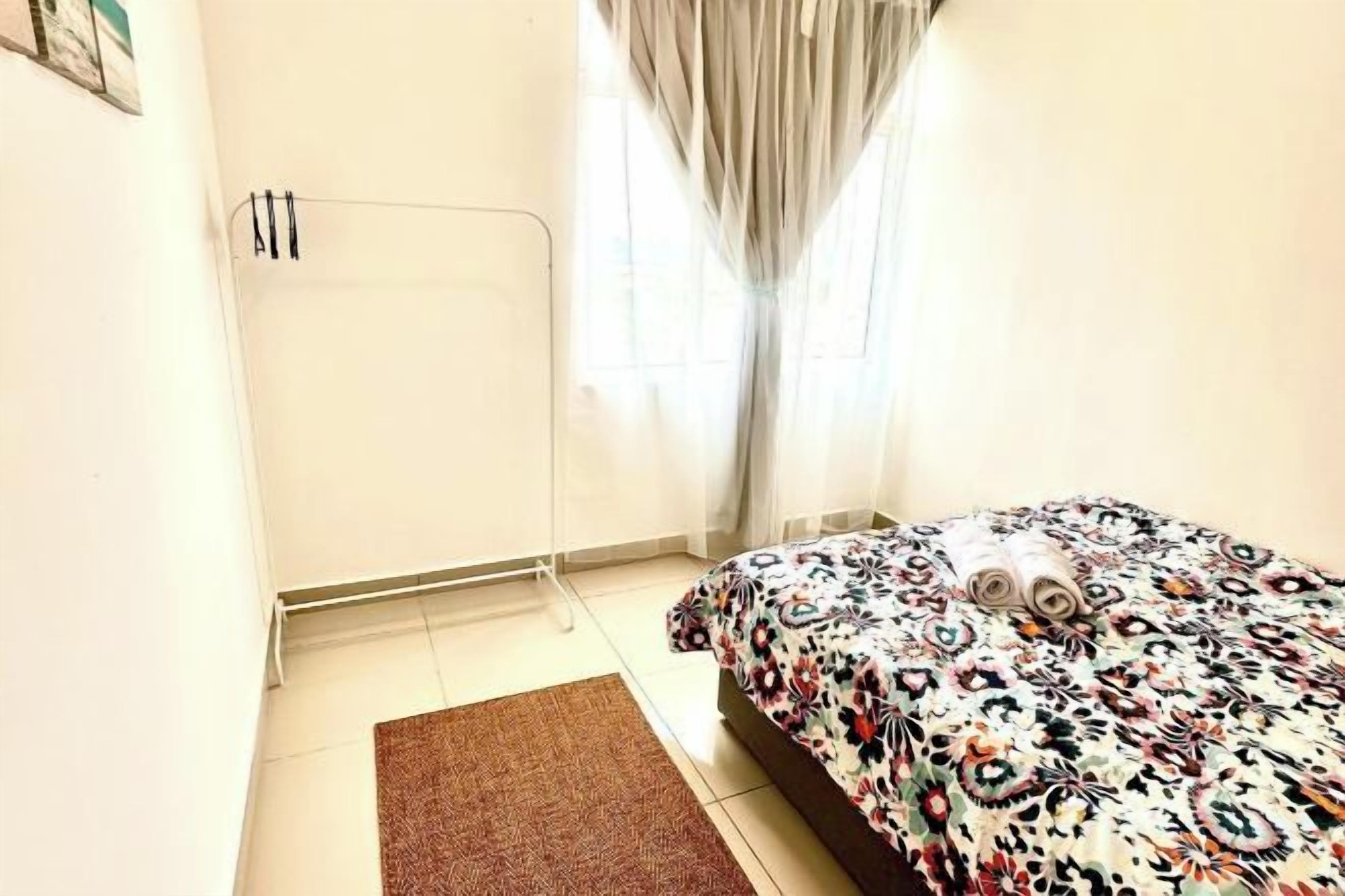 Quarto com cama, radiador, janela com cortinas e tapete castanho.