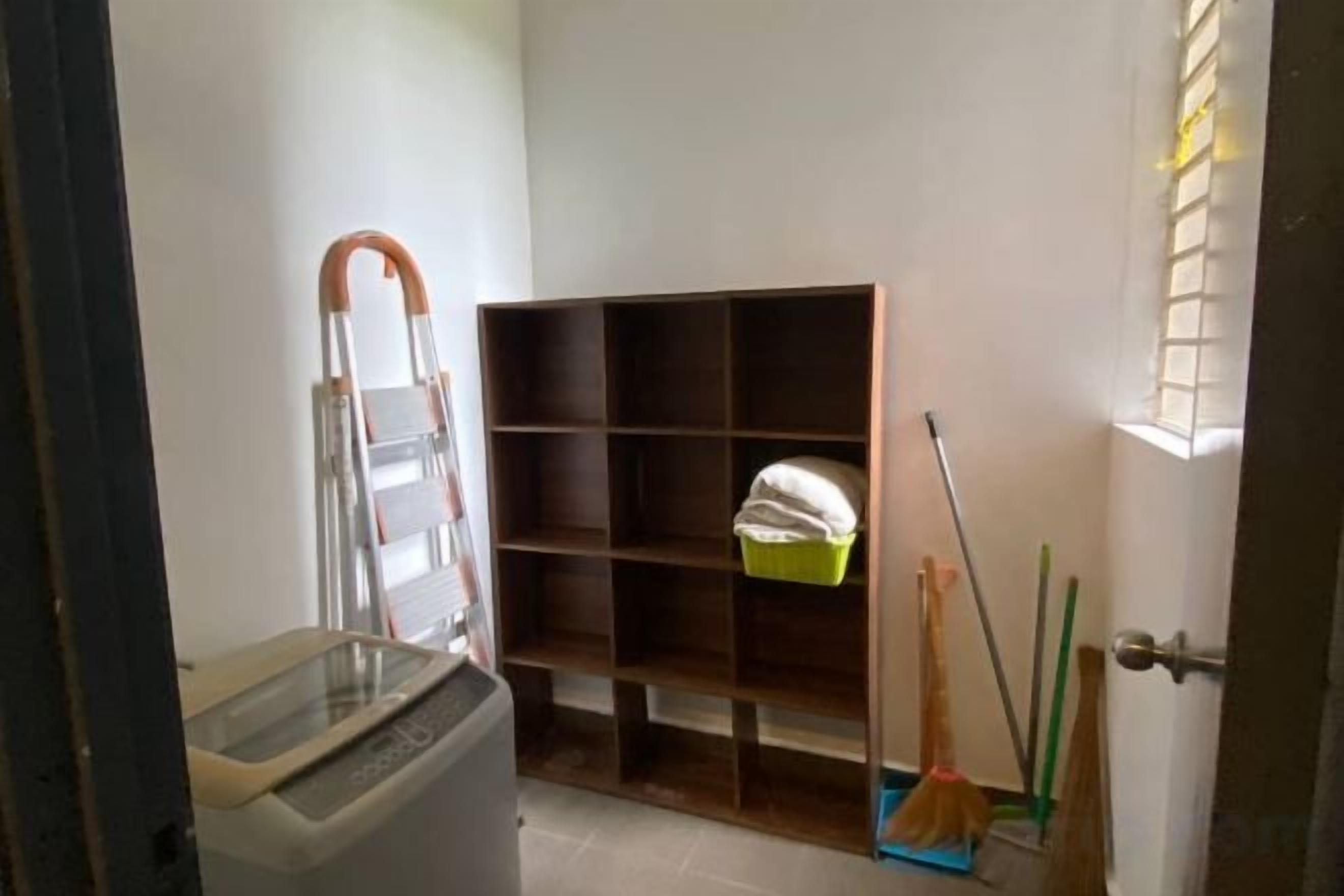 Un espace buanderie comprenant un lave-linge, un étendoir, un balai et une étagère avec des produits de nettoyage.