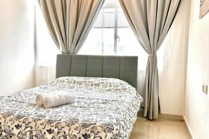 A neatly made bed with a patterned bedspread, a headboard, and curtains on a window. - Casa Budi Dwiputra 15 Putrajaya (Putrajaya)