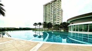 A swimming pool with a curved edge, a tall building in the background, and a palm tree to the left. - Casa Budi Dwiputra 15 Putrajaya (Putrajaya)