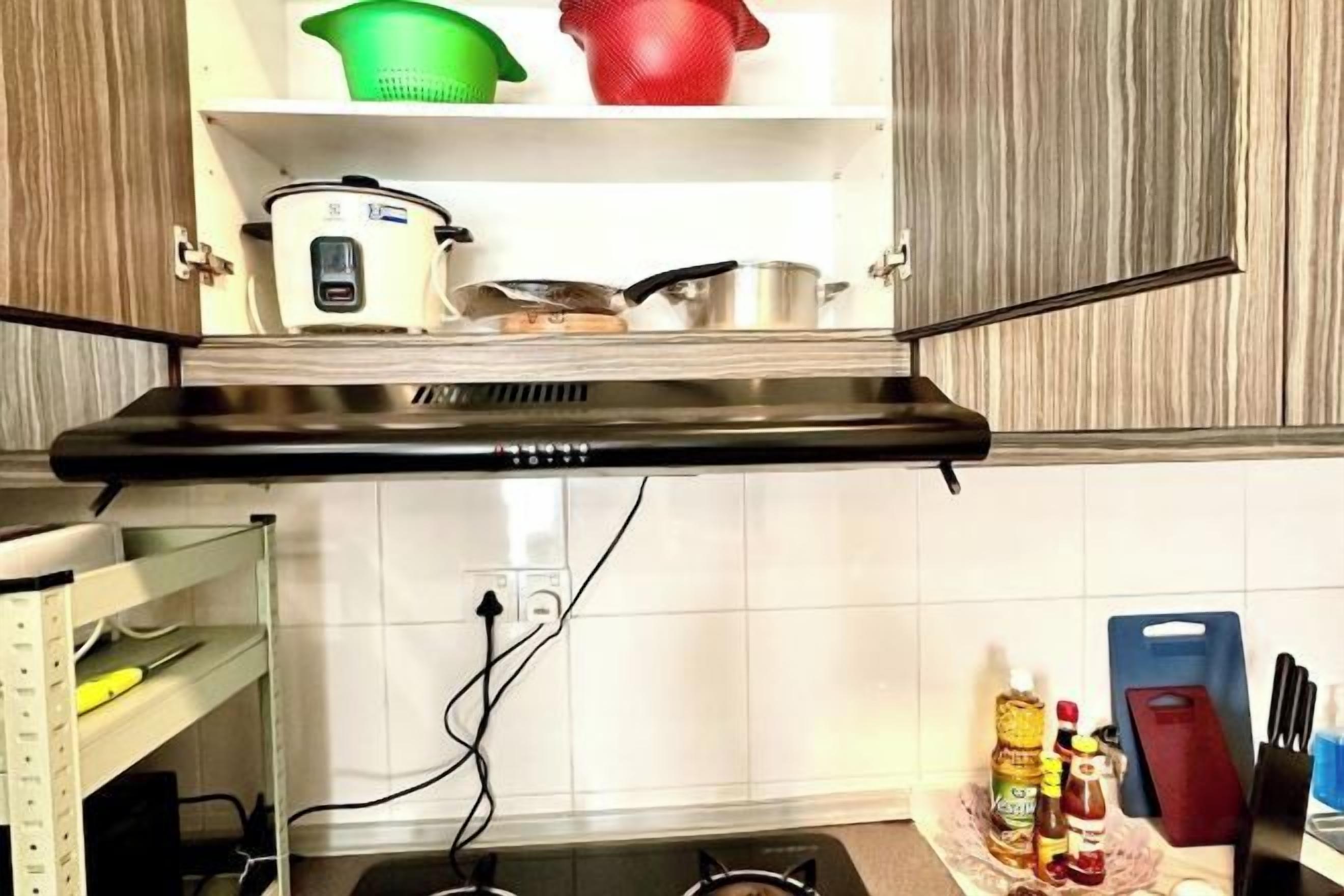 Cozinha com exaustor preto, armários brancos e diversos utensílios em prateleiras.