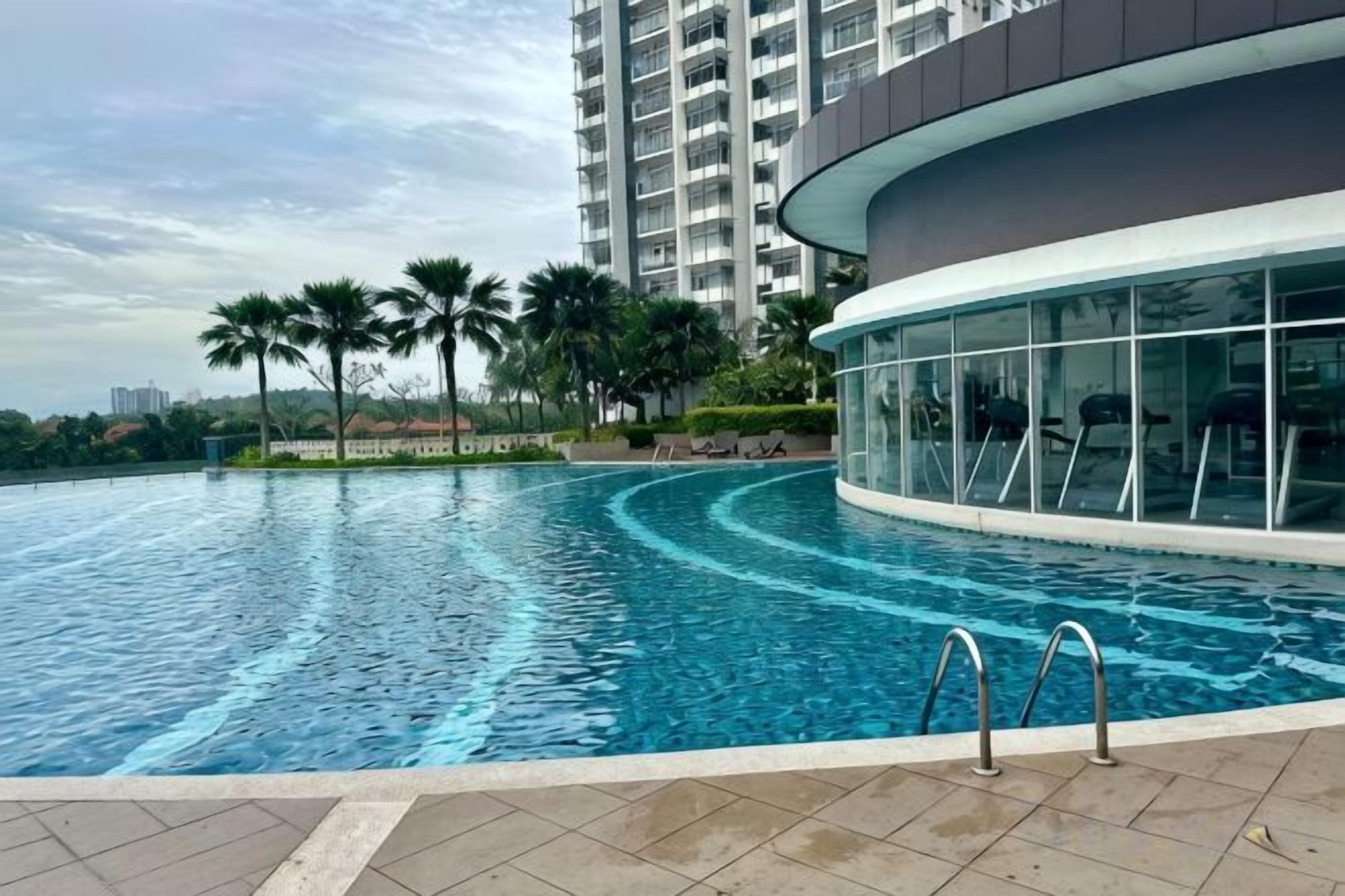 Une piscine à bord incurvé, entourée d’un bâtiment moderne doté de grandes fenêtres et d’un balcon.