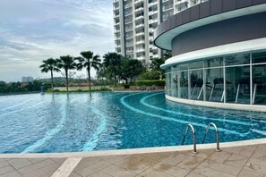 Ein Schwimmbecken mit geschwungener Kante, umgeben von einem modernen Gebäude mit großen Fenstern und einem Balkon.