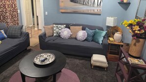 A living room with a dark grey sofa, a round coffee table, and a painting of a pier on the wall.