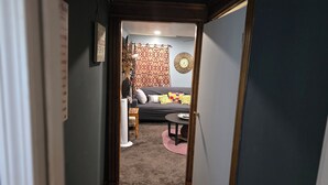 A narrow hallway leading to a living room with a sofa, a coffee table, and a rug.