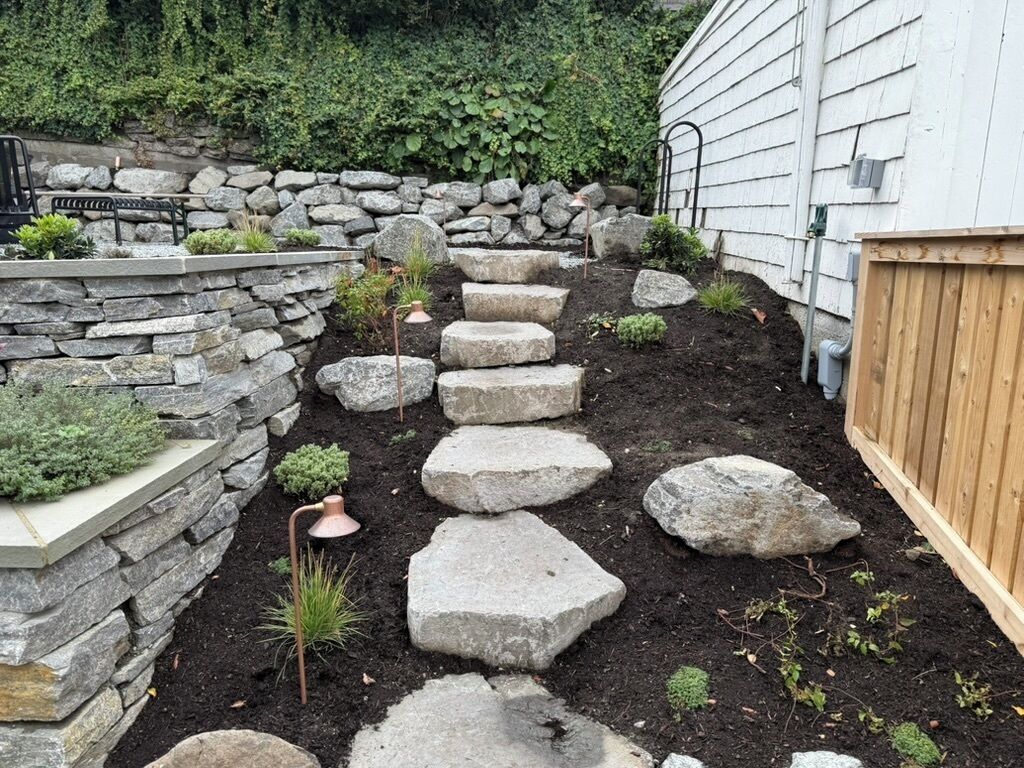 Un jardin avec un chemin en pierre, une clôture en bois et un mur de pierres.