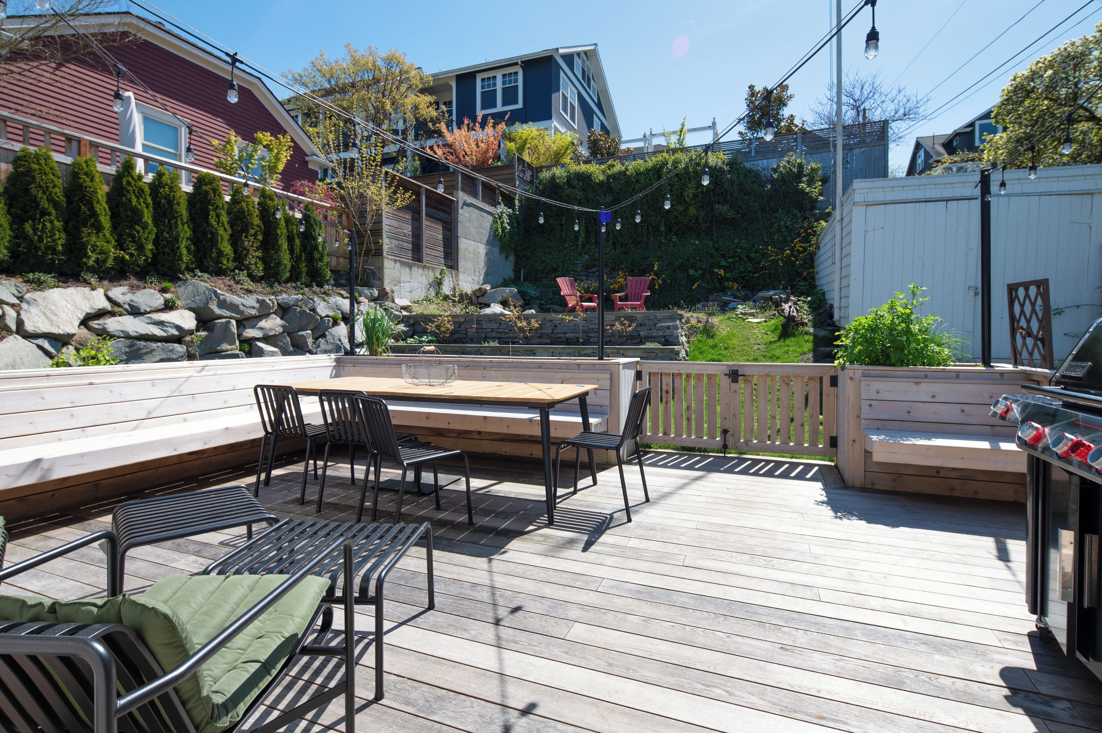 Une terrasse en bois avec une table et des chaises, un barbecue et un mur en pierre.