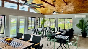 Une pièce spacieuse avec un plafond haut, de grandes fenêtres, un ventilateur de plafond et un coin repas comprenant une table et des chaises.