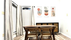 A dining area with a wooden table and chairs, a radiator, and three wall-mounted artworks.
