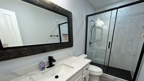 A bathroom with a white marble sink, a black faucet, a white toilet, and a glass shower enclosure.