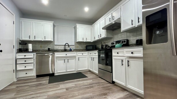 A modern kitchen with white cabinets, stainless steel appliances, and a herringbone wood floor.