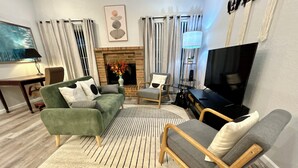 A modern living room with a green sofa, a grey armchair, a fireplace, a television, and a striped rug.