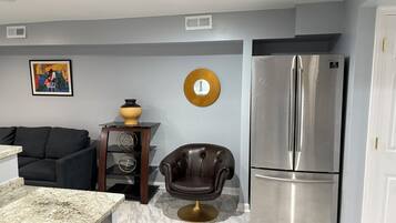 A modern kitchen with a marble countertop, a black leather chair, a stainless steel refrigerator, and a wall-mounted clock.