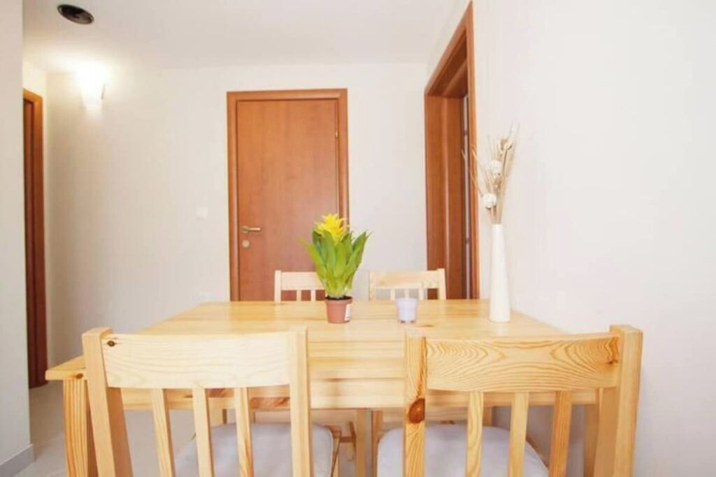 Una mesa de madera para comer con cuatro sillas, una planta en maceta y un jarrón con flores secas.