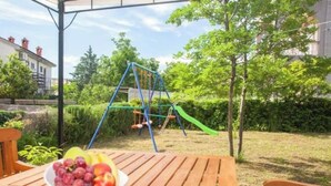 A wooden table with a bowl of fruit and a swing set in a garden. - 14Person Combination Apartment 4 Apartments Combined (Jadranovo)
