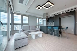 A modern living room with a grey sofa, a white coffee table, and a bar area with stools.