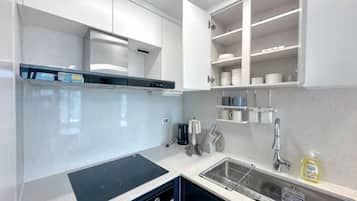 A modern kitchen with white cabinets, a black induction cooktop, and a stainless steel sink.