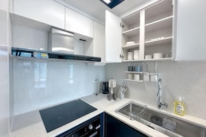A modern kitchen with white cabinets, a black induction cooktop, and a stainless steel sink. - The First Ocean Songdo (Busan)