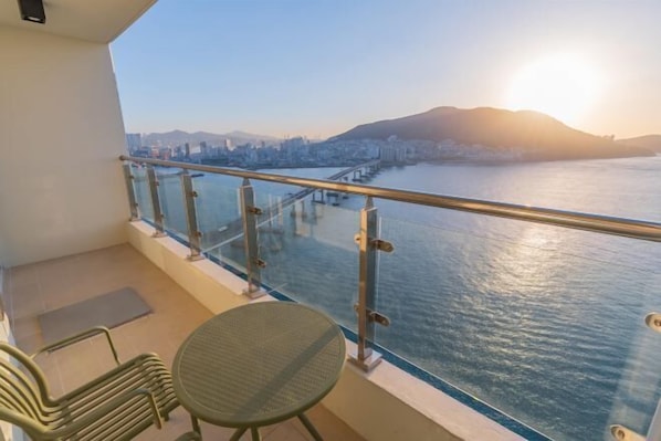 A balcony with a view of a river and a cityscape, featuring a table and chairs.